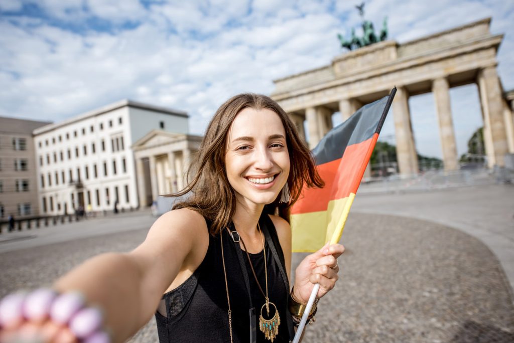 Mujer sosteniendo bandera de Alemania en Puerta de Brandeburgo, haciendo referencia a los intercambios en Alemania.
